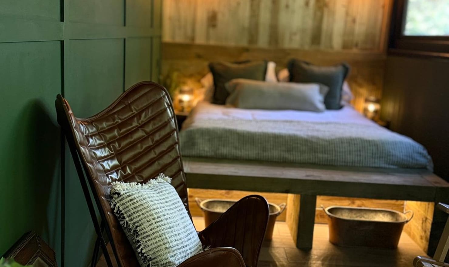 The Bolt Hole at Coast and Castles in the evening — warm amber lighting, leather butterfly chair and lush green interior