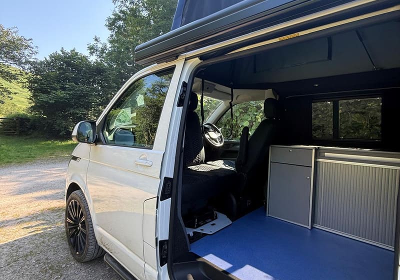 Cuddy with side door open and outdoor mat at a campsite