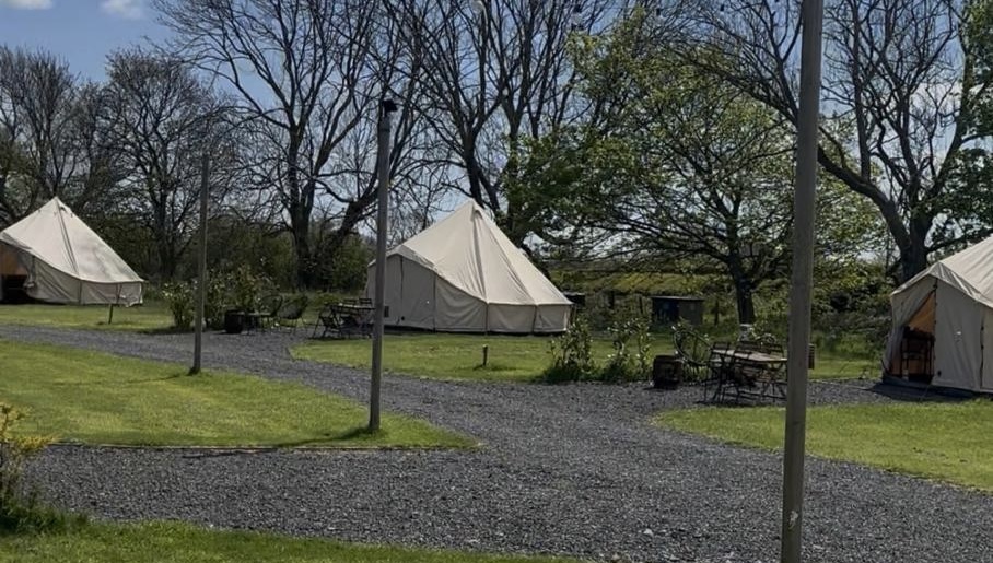 Bell tents on the glamping field at Coast and Castles, each with fire pit and outdoor seating